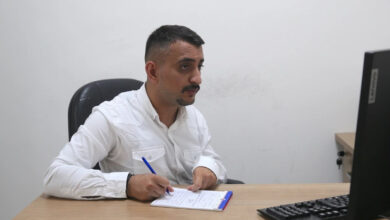 Bedensel engelli Yaşar Gültekin, masa başında oturarak ve bilgisayarda yer alan şeyleri önünde duran not defterine yazıyor.