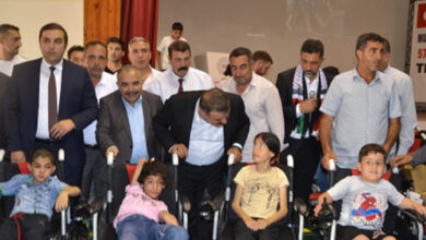 Etkinlikte engelli çocuklara hediye edilen akülü tekerlekli sandalye dağıtım töreninde protokol ve katılımcılar toplu fotoğraf çekimi için birlikte poz veriyorlar.