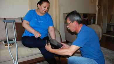 Postpolio sendromu olan engelli birey Mürvet Mızraklı koltukta oturuyor ve eşi Hüseyin Mızraklı dizinin üstünde durarak ayakkabı giydiriyor.