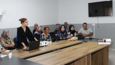 Engelli bireylerin aileleri sandalyelerde oturup yapılan sunumu izliyorlar. Sunumu yapan Psikolojik Danışman Yaren Çulcu, masanın üzerine atmış olduğu dizüstü bilgisayardaki sunumu karşısındaki bir ekrana yansıtıyor.