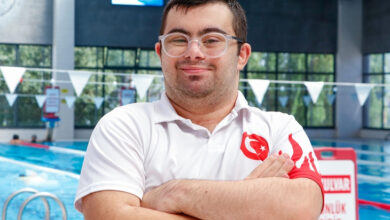 Down sendromlu birey Berkay Orak, yüzme havuzu başında milli forma giymiş şekilde, ellerini bağlayarak ayakta duruyor.