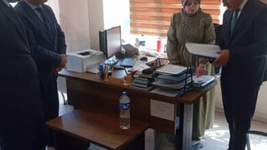 Fotoğrafta, mavi kaplı bir dosyayı inceleyen Aile ve Sosyal Politikalar Bakanlığı çalışanı ve inceleme yapılan birimdeki personel evrakları gösteriyor.