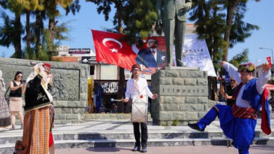Fotoğrafta, iki engelli birey karşılıklı şekilde zeybek oynuyor. Engelli bireylerin ortasında bir davulcu var ve davul çalıyor. Etkinliğe katılan kişilerde izliyor.