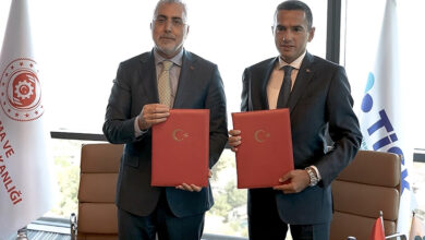 Çalışma ve Sosyal Güvenlik Bakanı Vedat Işıkhan ve TİSK Başkanı Özgür Burak Akkol ile yan yana ve ellerinde kırmızı kaplı protokol anlaşmasını tutuyorlar.