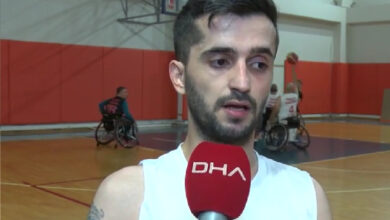 Fotoğrafta, tekerlekli sandalye basketbol oyuncusu Halil Şahin, kırmızı renkli üzerinde DHA yazan mikrofona konuşuyor. Arka tarafta ise diğer tekerlekli sandalye basketbol oyuncuları antrenman yapıyor.