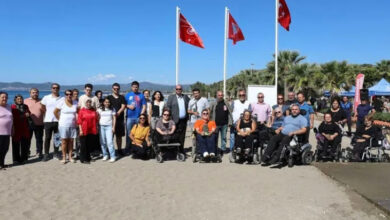 Fotoğrafta, engelli bireyler ve aileleri kumsalda kırmızı bayrak töreninde bir araya gelmişler.
