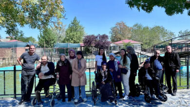 Tekerlekli sandalye kullanıcısı engelli bireyler ve farklı yeti kayıpları yaşayan engelli bireyler, bakım merkezi görevlileri ile birlikte fotoğraf çekimine katılıyorlar.