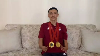 Paralimpik sporcu Umut Ünlü, evinde koltuk üzerinde oturarak ve boynunda Paris 2024 Paralimpik Oyunları’nda kazandığı 2 altın madalya asılı şekilde poz veriyor.