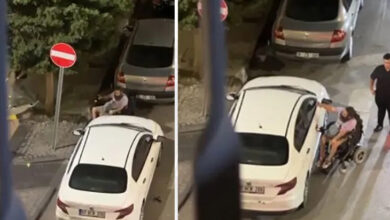 Fotoğrafta, tekerlekli sandalye kullanan engelli birey, beyaz renkli bir otomobilin çeşitli yerlerini kırıyor.