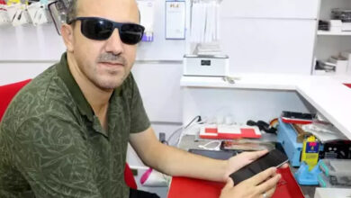 Görme engelli birey Ümit Çetin, gözünde siyah bir gözlük var ve elinde tuttuğu siyah telefonu inceliyor.