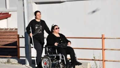 Akülü tekerlekli sandalye üzerinde yürüme engelli Nurcan Sivri oturuyor ve arkasında bulunan görme engelli Çiler Kocaman'a rehberlik ediyor.