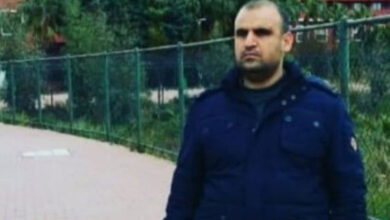 Fotoğrafta, görme engelli birey Mehmet Yıldırım bir yoldaki kaldırım üzerinde arkasında tellerin olduğu bir alanda fotoğraf çekiliyor.