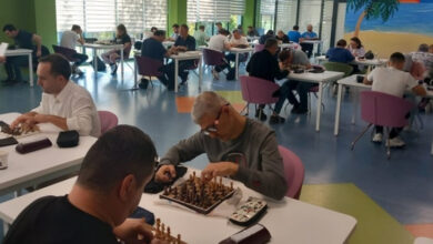 Görme engelli bireyler satranç takımlarıyla birlikte masaların etrafında oturarak turnuvaya katılıyorlar.