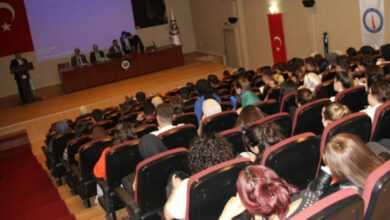 Kütahya Dumlupınar Üniversitesi'nde düzenlenen engelli farkındalığı etkinliğinden bir fotoğraf. Fotoğrafta konferans salonunda öğrenciler koltuklarda oturuyor ve sahnede yer alan bir konuşmacıyı dinliyorlar.