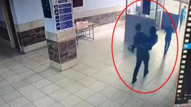 Fotoğrafta bir öğretmen, engelli öğrencisini kucağında dışarıya taşıyor. Öğretmen ve öğrencinin bulunduğu alanı işaretleyebilmek için kırmızı bir halka çizilerek içine alınmışlar.