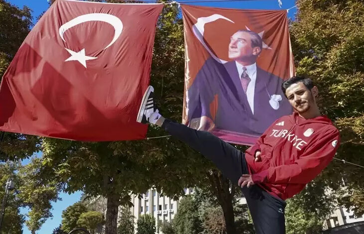 Para milli tekvandocu Mahmut Bozteke, tek ayağını havaya kaldırarak poz veriyor. Arkasında Türk bayrağı ve üzerinde Mustafa Kemal Atatürk olan bir başka bayrak daha asılı.