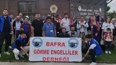 Fotoğrafta, görme engelli bireyler ellerinde beyaz baston tutarak, Bafra Görme Engelliler Derneği yazan bir pankartın arkasında ayakta duruyorlar.