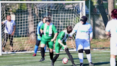 Gözlerinde siyah bant takılı olan kadın futbolcular, futbol sahasında mücadele ediyorlar.
