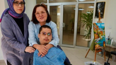 Engelli birey Bünyamin Tok, tekerlekli sandalye üzerinde oturuyor. Arkasında babaannesi ve yanlarında ise resim öğretmeni yer alıyor.