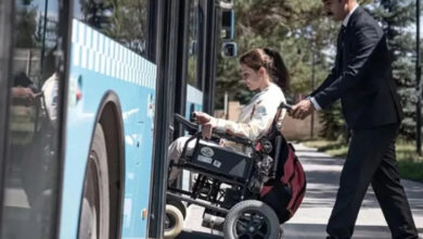 Fotoğrafta, akülü tekerlekli sandalye kullanıcısı engelli bir birey belediye otobüsüne biniyor. Tekerlekli sandalyenin geçebilmesi için engelli rampası kaldırıma doğru indirilmiş ve rampanın üzerinden engelli birey aracını geçirerek otobüsün içerisine biniyor.
