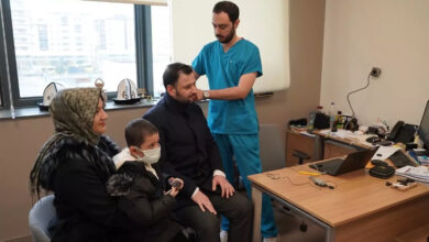 Fotoğrafta, muayenehane odasında evli bir çift sandalyede oturuyor. Doktor ise kulaklarını muayene ediyor.