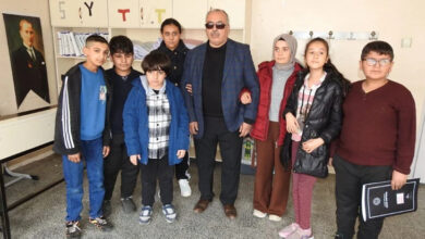 Görme engelli öğretmen Ekrem Kılıç ve görme engelli öğrencileri ile birlikte sınıfın ortasında ayakta duruyorlar. Öğrencilerin bazıları öğretmenin koluna girerek ayakta bekliyorlar.