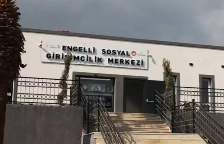 Fotoğrafta, "Engelli Sosyal Girişimcilik Merkezi" yazılı bir tabelanın asılı olduğu bina var. Binanın girişinde birçok merdiven olduğu görülmektedir.