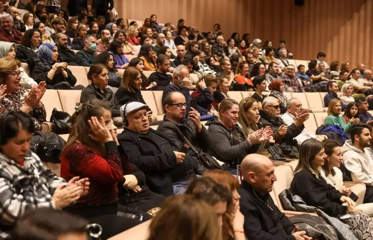 Fotoğrafta, engelli bireyler tiyatro salonunda izleyici koltuklarında oturuyorlar. Görme engelli bireyler için betimlemeleri duymaları adına kulaklıklar dağıtılmış. İşitme engelli bireyler ise yazı tahtasından betimlemeleri ve konuşmaları görüyorlar.