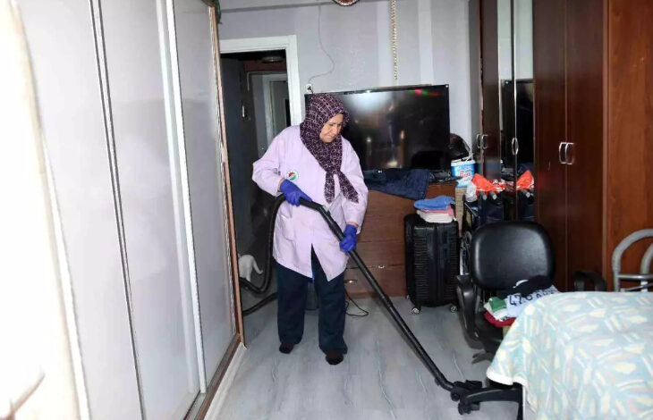 Fotoğrafta, Kepez Belediyesi'nin evde sağlık hizmeti ekibinin temizlik konusunda da destek olduğu görülüyor. Görevlinin elinde elektrikli süpürge ile evi süpürüyor.