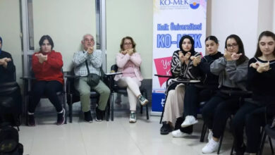 Fotoğrafta, bir sınıfta işaret dili öğrenen insanlar var. Tek kişilikli sıralarda oturan insanlar Eğitmen eşliğinde işaret dili öğreniyor.