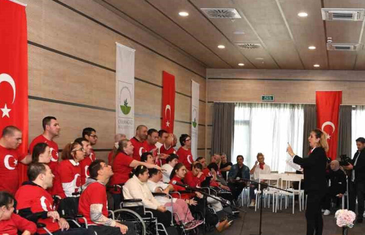 Fotoğrafta, farklı yeti kaybolan engelli bireyler birlikte koro ekibi içinde şarkı söylüyorlar. Engelli bireyleri etkinliğe katılan kişiler ve aileleri dinliyor.Engelli bireylere Türk bayrağındaki ay ve yıldızın olduğu kırmızı renkli tişörtler giydirilmiş.