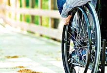 Fotoğrafta, tekerlekli sandalye kullanan engelli birey belden aşağısı gözüküyor. Tekerlekli sandalyenin tekerlerinden iterek hareket edebiliyor.
