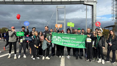 46. İstanbul Maratonunda koşan bir grup elinde yeşil renkli “Hatay'daki engelli çocukların kahramanı ol” yazılı bir pankartla farkındalık etkinliği düzenliyor.