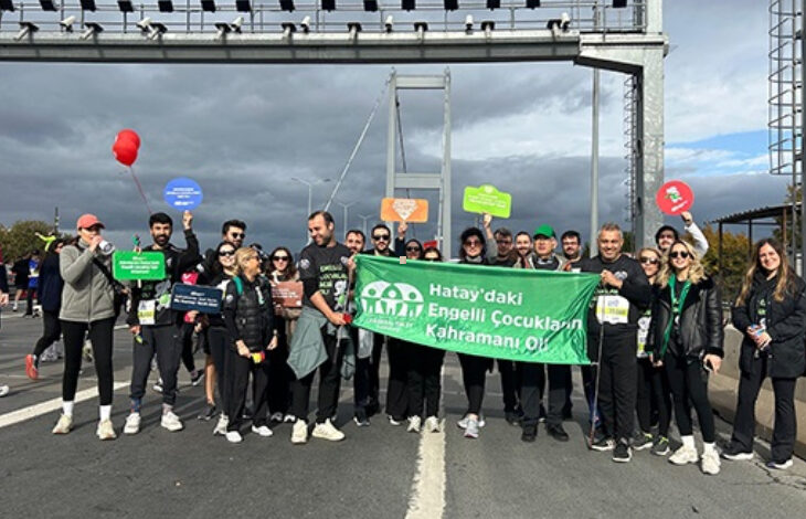 46. İstanbul Maratonunda koşan bir grup elinde yeşil renkli “Hatay'daki engelli çocukların kahramanı ol” yazılı bir pankartla farkındalık etkinliği düzenliyor.