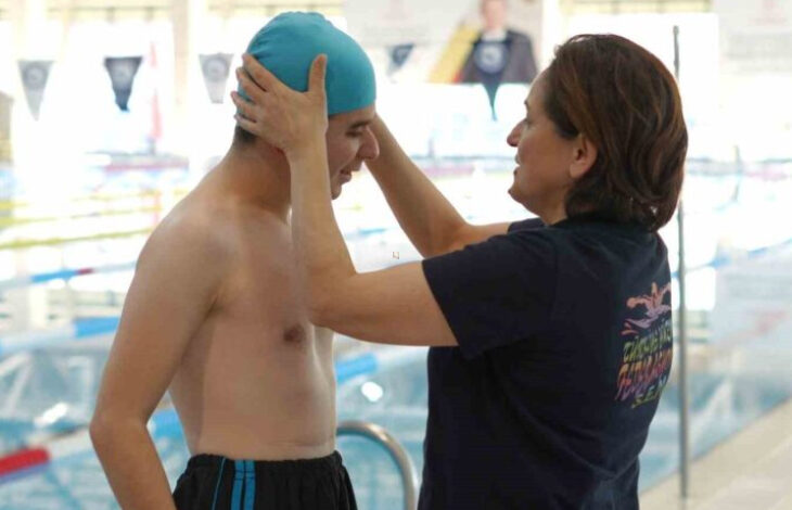 Fotoğrafta, havuzun kenarında yüzme sporcusu engelli birey Enes Emin Şener'in başına annesi yüzme bonesini takıyor.