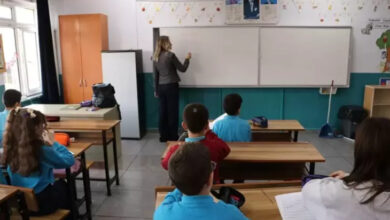 Fotoğrafta bir sınıfta öğrenciler ve bir öğretmen var. Öğrenciler sıralarında oturuyor. öğretmen tahtada bir şeyler yazıyor. Tahtadaki öğretmen engelli birey Melis Aracı olduğu görülüyor.