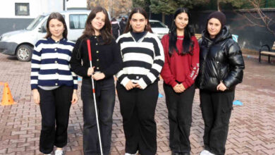 Fotoğrafta, bir okulun bahçesinde ayakta duran 5 kız öğrenci var. Öğrencilerden birinin elinde görme engelli bireylerin kullandığı beyaz baston olduğu görülüyor.