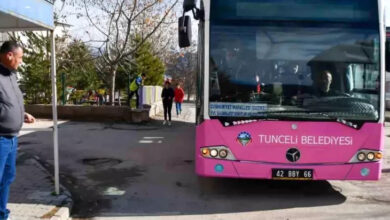 Mor renkli büyük bir toplu taşıma amacıyla kullanılan otobüs durağa doğru yaklaşıyor. Durakta ise insanlar otobüsü bekliyor.
