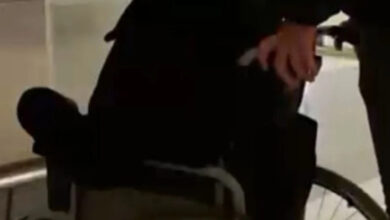 Tekerlekli sandalye üzerinde oturan engelli birey ve tekerlekli sandalyeyi arkasındaki bölümden iterek hareket ettiren yakını var. Engelli birey ve yakınının yüzü gözükmüyor.