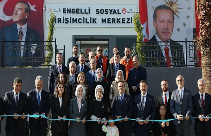 Fotoğrafta Hatay Engelli Sosyal Girişimcilik Merkezi binası önünde toplanmış bir kalabalık var. Toplanan kalabalığın arasında Emine Erdoğan, Mahinur Özdemir Göktaş, Mehmet Kacır gibi isimler var.