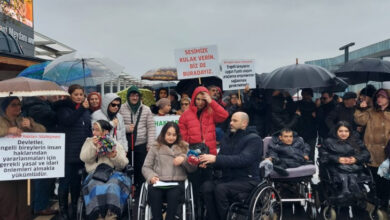 Fotoğrafta, engelli bireyler yağmurlu bir havada tekerlekli sandalyeleri üzerinde oturarak ve bazılarının elinde pankartlarla birlikte basın açıklamasına katılıyorlar.