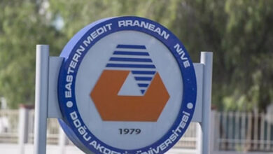 Bu görselde, Doğu Akdeniz Üniversitesi'ne (DAÜ) ait bir tabela veya logo yer almaktadır. Logo, yuvarlak bir çerçeve içerisinde tasarlanmış ve üst kısmında İngilizce "Eastern Mediterranean University" (tam olarak "Eastern Mediterranean University" ibaresinin tamamlanmamış olduğu anlaşılıyor) yazısı yer alıyor. Alt kısmında ise Türkçe "Doğu Akdeniz Üniversitesi" ibaresi bulunuyor. Logonun merkezinde, turuncu bir altıgen şekil ile mavi renkli, şeritler şeklinde bir grafik tasarım yer alıyor. Alt kısımda, üniversitenin kuruluş yılı olan "1979" yazısı bulunmakta. Logo, mavi, turuncu ve beyaz renk temalarını içeriyor ve arka planda bulanık bir açık hava sahnesi görülüyor.