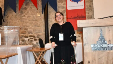 Fotoğrafta, İzmir Kent Konseyi Engelliler Meclisi Başkanlığına seçilen Şirince Süzek, kürsüde beyaz renkli koltuk değnekleri ile ayakta duruyor.