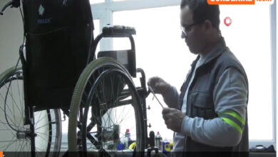 Fotoğrafta, bir tamirhanede çalışan bir adam tekerlekli sandalye tamir etmektedir. Adam, elinde bir alet tutarak dikkatlice tekerlekli sandalyeyi kontrol ediyor. Üzerinde reflektör şeritli iş yeleği ve gözlük bulunuyor. Arka planda tamirhanenin düzenli bir ortamı ve pencere görülüyor. Fotoğrafın alt kısmında “Nilüfer’de Engelli Bireyler İçin Tekerlekli Sandalye Tamir Hizmeti” yazısı yer almakta, üst köşede ise bir haber sitesi logosu dikkat çekiyor. Bu kare, engelli bireylerin ihtiyaçlarına yönelik toplumsal destek ve hizmetlerin önemini vurgulayan bir anı yansıtıyor.