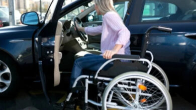 Tekerlekli sandalye kullanan engelli kadın otomobil sürücüsü, araca binmek için kendini taşımaya çalışıyor. Tekerlekli sandalye otomobilin yakınında ve direksiyondan tutarak içeriye doğru girmeye çalışıyor.