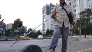 Fotoğrafta görme engelli birey Serhat Esen, elindeki beyaz baston ile kaldırımda yürümeye çalışıyor. Kaldırımın uç kısmında koruyucu amaçla yapılmış mantar şeklinde büyük bir taş var.
