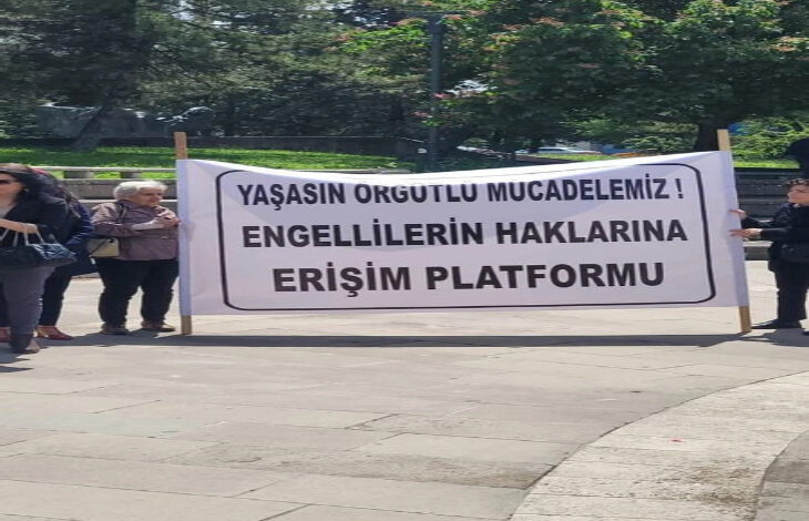 Fotoğrafta bir grup insan, açık bir alanda bir pankart tutuyor. Pankartta şu yazı bulunuyor: "Yaşasın Örgütlü Mücadelemiz! Engellilerin Haklarına Erişim Platformu". Arka planda ağaçlar ve yeşil bir alan yer alıyor. Görsel, engelli haklarıyla ilgili bir protesto veya farkındalık etkinliğini yansıtıyor. Toplumsal dayanışma ve hak arayışı mesajı ön planda.