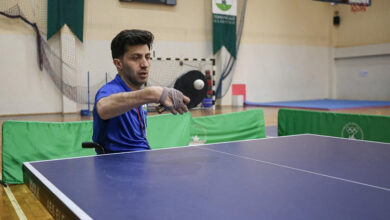 Görselde, tekerlekli sandalyede oturan bir sporcu, bir spor salonunda masa tenisi oynuyor. Orhan Koca’nın, geçirdiği trafik kazasının ardından masa tenisine yönelerek ilk madalyasını kazandığı anları yansıtan bir kare.