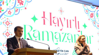 Fotoğrafta bir etkinlik sahnesi görülüyor. Sol tarafta takım elbise giymiş bir erkek konuşma yaparken, sağ tarafta bir kadın işaret diliyle çeviri yapıyor. Arkadaki büyük ekranda "Hayırlı Ramazanlar" yazısı ve süslemeler bulunuyor. Ekranın altında "Hüseyin Can Güner, Çankaya Belediye Başkanı" ifadesi yer alıyor.