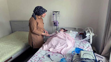 SMA'lı Elanur cihazlara bağlı yatağında uzanıyor ve annesi ayakta durarak elini tutuyor.